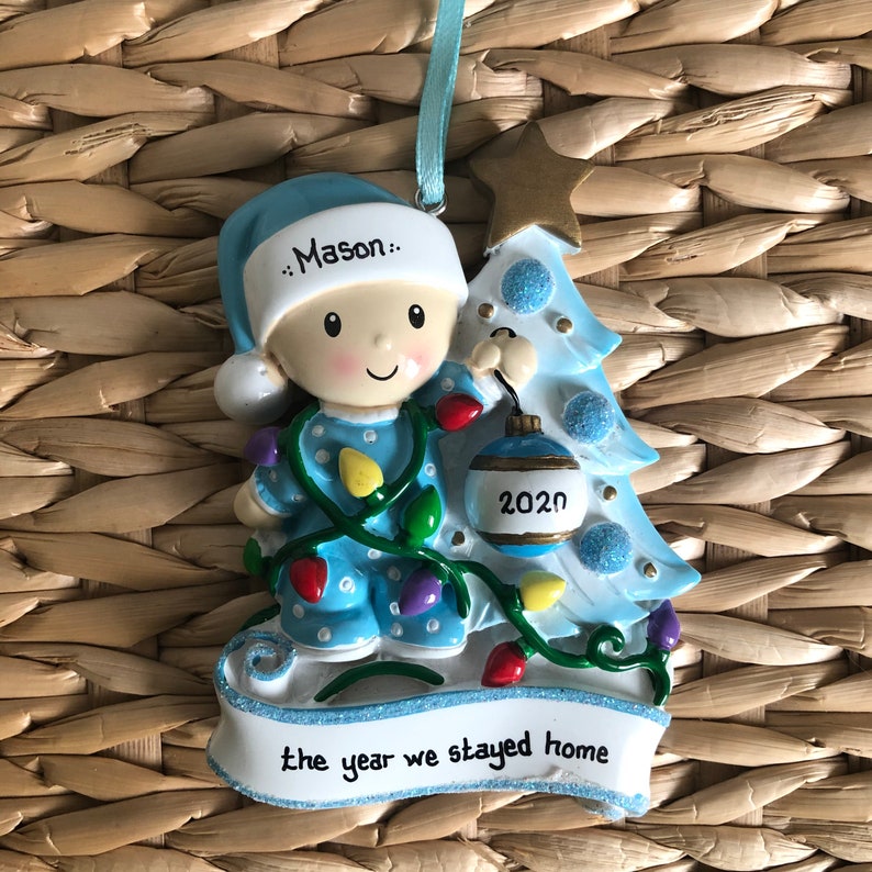 May include: A blue and white Christmas ornament featuring a baby boy in pajamas holding a blue ornament with the year 2020 on it. The ornament is decorated with a blue Christmas tree and lights. The text "the year we stayed home" is on the bottom of the ornament.