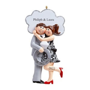 Może przedstawiać: Ozdoba choinkowa z personalizacją przedstawiająca kreskówkową parę, która się obejmuje, a kobieta trzyma pierścionek. Ozdoba jest ozdobiona srebrnym pierścionkiem i tekstem "She Said Yes!" oraz "2022". Ozdoba w kształcie chmury zawiera również imiona "Philip & Laura".