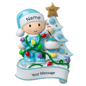 May include: A blue baby ornament holding a blue and white ornament and wearing a blue and white pajamas with colorful lights. The ornament is hanging from a blue and white Christmas tree with a gold star on top. The ornament has a banner that says "Your Message" and a space for a name and year.