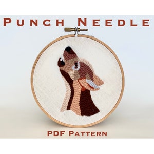 May include: A punch needle pattern featuring a howling wolf in shades of brown, peach, and white. The pattern is displayed in a wooden embroidery hoop. The text "Punch Needle" and "PDF Pattern" are printed below the hoop.
