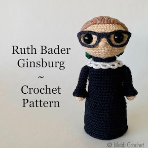 Op de afbeelding: Gehaakte pop van Ruth Bader Ginsburg, met een zwarte bril, een witte kanten kraag en een zwarte jurk. De pop heeft lichtbruin haar en groene oorbellen. Tekst links luidt "Ruth Bader Ginsburg ~ Crochet Pattern."