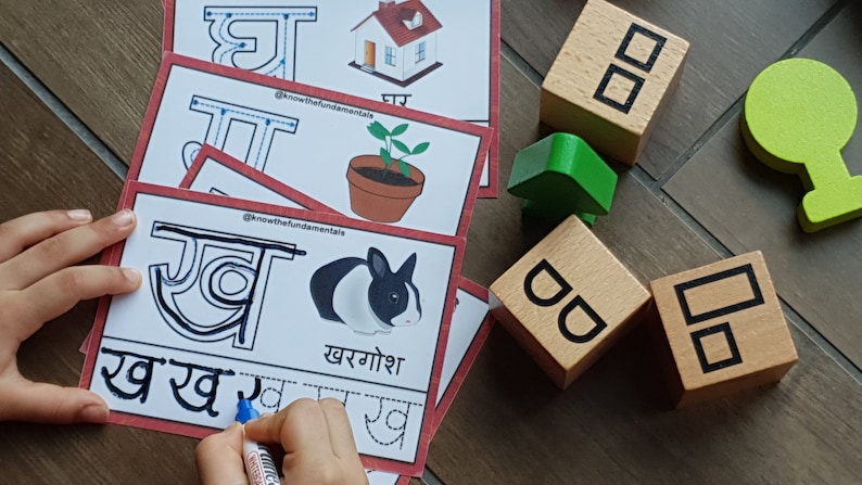 May include: A child's hand traces the Hindi letter 'र' (ra) on a white card with red borders. The card features a black and white rabbit and the word 'खरगोश' (khargoosh) which means rabbit in Hindi. The card also includes a dotted line for tracing the letter.