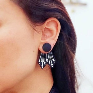 Może przedstawiać: Geometriczne kolczyki w kolorze czarnym i białym z okrągłym czarnym elementem. Kolczyki są wykonane z drewna i mają nowoczesny design.