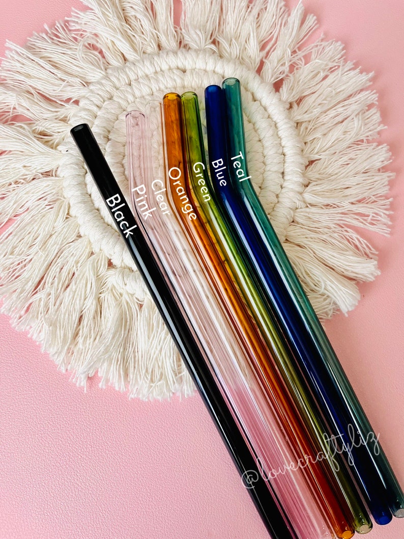 Pu&ograve; includere: Set di sette cannucce da bere in vetro di vari colori, tra cui nero, trasparente, rosa, arancione, verde, blu e turchese. Le cannucce sono disposte a ventaglio su un sottobicchiere di uncinetto bianco.