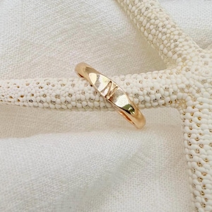 May include: A polished rose gold ring featuring a single engraved letter N on the front surface. The band has a smooth, rounded profile and a reflective metallic finish, resting against a textured, off-white starfish surface.