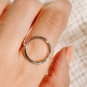 Puede incluir: Un anillo de oro con un diseño simple de círculo. El anillo se lleva en un dedo.