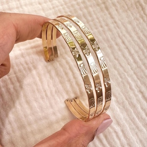 May include: Three gold-toned bracelets with a delicate design of seashells and starfish. The bracelets are stacked on top of each other.