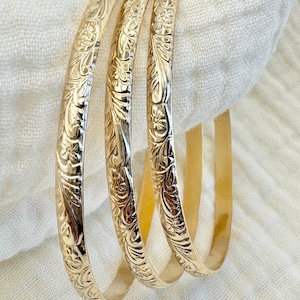 May include: Three gold bangle bracelets with an intricate floral design.