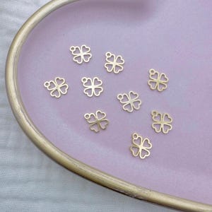 Può includere: Primo piano di un piatto rosa a forma di cuore con nove ciondoli a forma di quadrifoglio dorati.