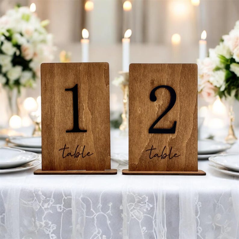 May include: Two wooden table number signs with black numbers and the word "table" written in cursive. The numbers are 1 and 2.