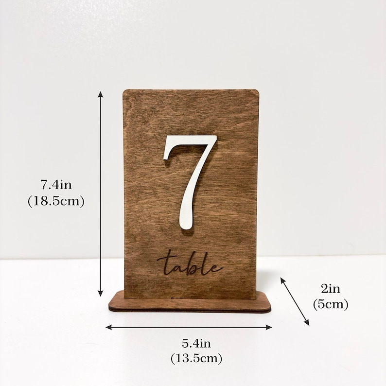 May include: A wooden table number with the number 7 and the word "table" engraved on it. The number is 7.4 inches tall and 5.4 inches wide. The base is 2 inches tall.