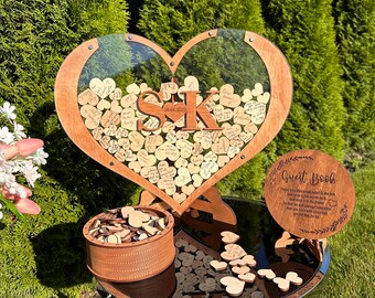 May include: A wooden heart-shaped guest book with a clear acrylic insert. The heart is filled with small wooden hearts that guests can write on. The heart is on a wooden stand. There is a small wooden box with more hearts and a sign that says "Guest Book".