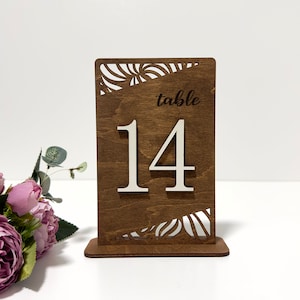 May include: Wooden table number with a decorative swirl design. The number 14 is displayed in white on a brown background. The text "table" is also displayed on the sign.