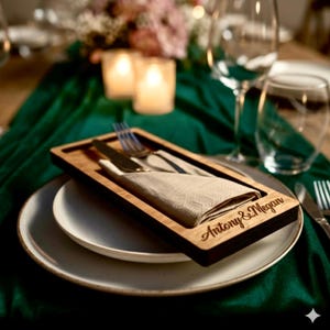 Puede incluir: Un juego de mesa de madera con un cuchillo, un tenedor y una servilleta doblada. El marco de madera está grabado con los nombres "Antony & Megan". El juego está sobre un plato blanco, con un mantel verde en el fondo.