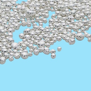 May include: A close-up of a pile of small, round, silver beads against a light blue background.