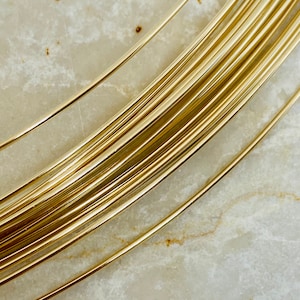 May include: Close-up of a bundle of shiny, golden-colored wire. The wire is tightly packed together, with individual strands visible. The wire appears to be smooth and reflective, catching the light. The background is a light, marbled surface.