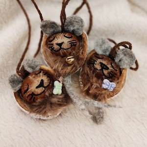 May include: Three brown nut shell cat ornaments with painted faces and fuzzy brown fur. Each cat has a different coloured button on its chest.