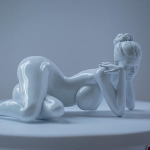 Pode incluir: Escultura de cerâmica branca de uma figura reclinada. A figura está pousada sobre uma superfície branca, com os braços cruzados e a cabeça apoiada nas mãos. A escultura tem um acabamento liso e brilhante.