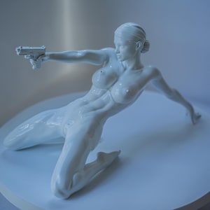 Pode incluir: Escultura branca de uma figura ajoelhada segurando uma arma, com um braço estendido. A figura está sobre uma superfície circular branca. A escultura tem um acabamento liso e brilhante, sobre um fundo suave.