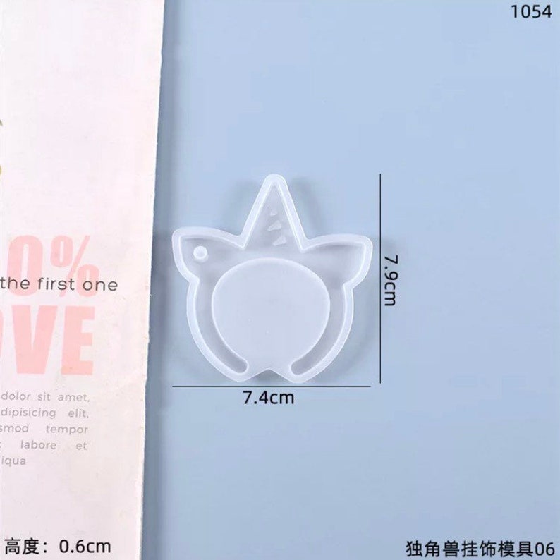 May include: A clear, unicorn-shaped mold for crafting. The mold measures 7.9 cm in height and 7.4 cm in width, with a thickness of 0.6 cm. The design includes a horn and a circular area for a face. The text "the first one" is visible.