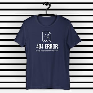 Könnte beinhalten: Marineblaues T-Shirt mit weißer Grafik eines toten Dokuments und dem Text "404 ERROR Sorry, motivation not found." Das T-Shirt hängt an einem schwarzen Kleiderbügel vor einem schwarz-weiß gestreiften Hintergrund.