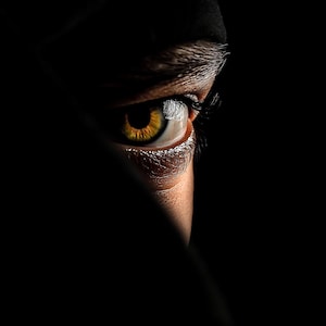 Puede incluir: Primer plano de un ojo humano con iris dorado, sobre un fondo negro. Se ve parte de la ceja y el párpado superior. La iluminación crea sombras y reflejos dramáticos, resaltando los detalles.