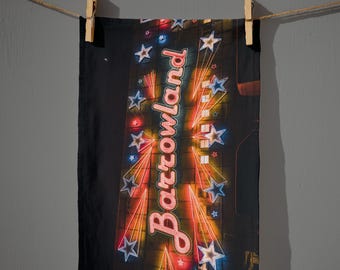 May include: Black towel with a neon sign design. The design features the word "Barrowland" in pink neon, surrounded by blue, red, and yellow stars and lines. The towel is hanging from a clothesline.