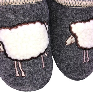 May include: A pair of gray wool slippers with white sheep embroidered on the front. The sheep have brown eyes and a brown nose.
