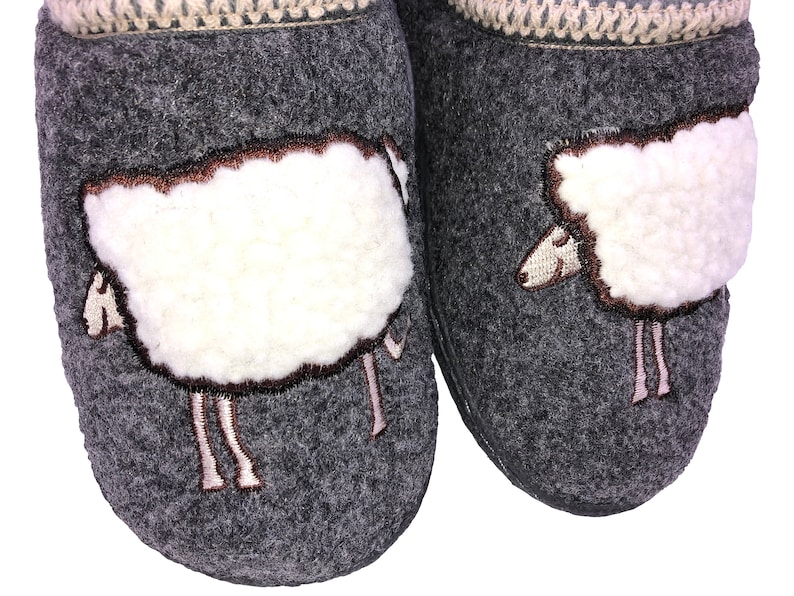 May include: A pair of gray wool slippers with white sheep embroidered on the front. The sheep have brown eyes and a brown nose.