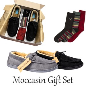 May include: A gift set containing a pair of grey and black moccasin slippers, a pair of black, red and white striped socks, and a pair of black socks with a red stag design. The slippers and socks are presented in a brown gift box.