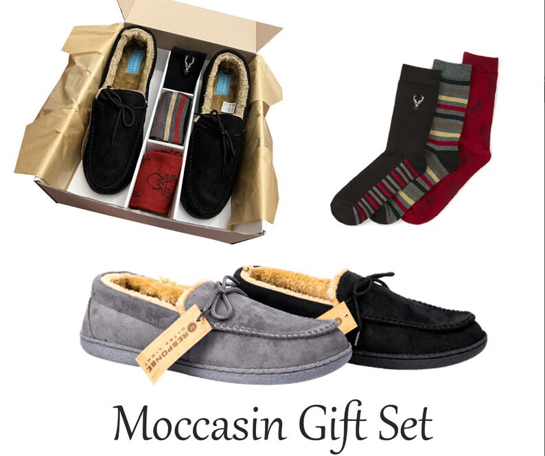 May include: A gift set containing a pair of grey and black moccasin slippers, a pair of black, red and white striped socks, and a pair of black socks with a red stag design. The slippers and socks are presented in a brown gift box.