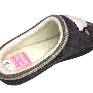 May include: Gray fleece slipper with a white and brown embroidered design. The slipper has a beige trim and a white fleece lining. The size 37 is visible on the inside of the slipper.