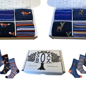 May include: Three pairs of socks in a box. The socks are blue and orange with a pattern of foxes and deer. The box is white with the words "SOX BOX" printed on it.