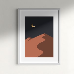 May include: A framed print of a minimalist desert landscape with a crescent moon in the night sky. The sand dunes are a warm orange color against a dark blue background.