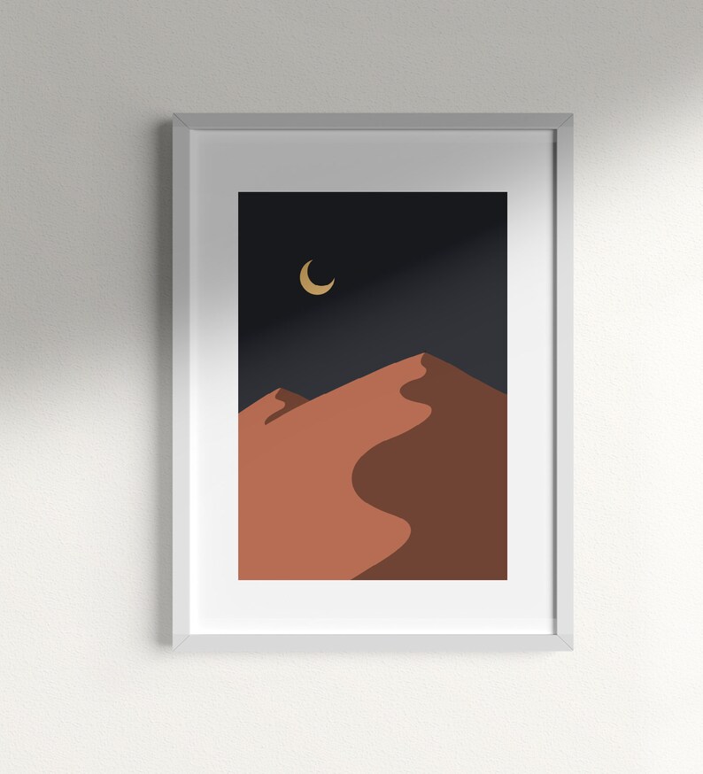 May include: A framed print of a minimalist desert landscape with a crescent moon in the night sky. The sand dunes are a warm orange color against a dark blue background.