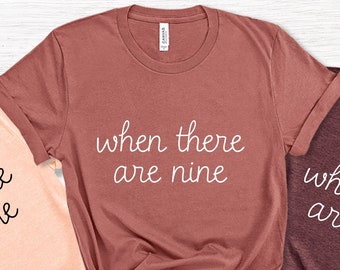 May include: Three t-shirts with the text "when there are nine" printed on them. The shirts are in peach, maroon, and dark grey.