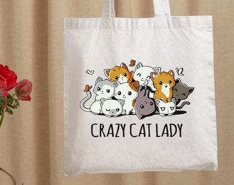 May include: White canvas tote bag featuring a graphic of a group of cartoon cats and the text "Crazy Cat Lady".