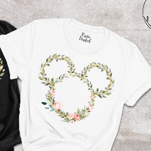 Peut inclure: T-shirts noirs et blancs avec un motif floral de Mickey Mouse. Le motif est une couronne de feuilles vertes et de fleurs roses. Les chemises sont pr&eacute;sent&eacute;es avec un jean bleu et des chaussures marron.