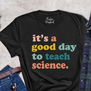 Op de afbeelding: Zwart T-shirt met de tekst "it's a good day to teach science." in regenboogkleuren.