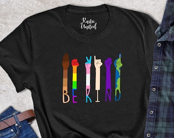 May include: Black t-shirt with a graphic of five hands in different skin tones making the sign language symbol for "be kind". The hands are each decorated with a different color stripe, including rainbow, white, black, blue, and green.