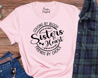 Könnte beinhalten: Rosafarbenes T-Shirt mit einem schwarzen Kreis-Motiv, auf dem "Cousins by Blood, Sisters by Heart, Friends by Choice" steht.