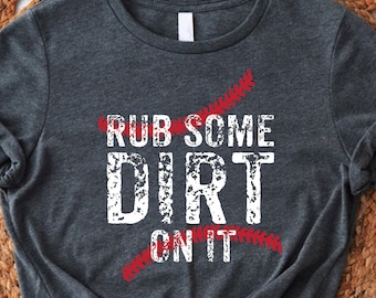 Può includere: Una maglietta grigia scura con una grafica bianca che dice "Rub Some Dirt On It" con un design a punto di cucitura da baseball rosso.