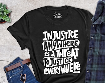 Pode incluir: Camiseta preta com texto branco que diz "Injustiça em qualquer lugar é uma ameaça à justiça em todos os lugares".