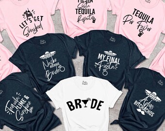 May include: Set of ten t-shirts with various designs and text related to a fiesta theme. The shirts are in pink and dark blue colors. The text on the shirts includes "Let's Get Smashed", "Tequila Lime & Sunshine", "My Final Fiesta", "Shake Your Maracas", "Nacho Average Bride", "Fiesta Cesta Tequila Reprints", "Tequila Por Favor", "Te:  Aye  Que", "Adios Bitchachos", and "Bride".