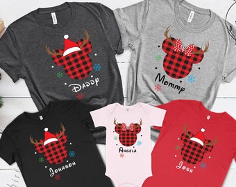 Peut inclure: Plusieurs t-shirts et un body sur le thème de Noël. Chaque vêtement présente une tête de Mickey Mouse à carreaux avec des bois et un bonnet de Père Noël. Les hauts sont de différentes couleurs, dont le gris, le noir et le rouge, avec des noms imprimés en dessous.