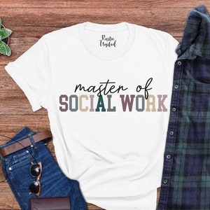 May include: White t-shirt with the text "master of SOCIAL WORK" in colorful letters. The shirt is laid out on a wooden surface with a pair of jeans, sunglasses, and a plaid shirt.
