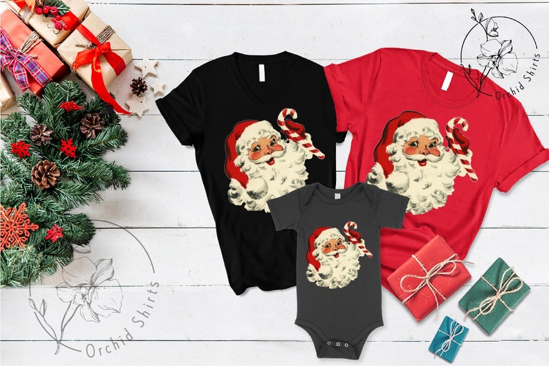 May include: A set of three Christmas shirts featuring a vintage illustration of Santa Claus holding a candy cane. The shirts are black, red, and gray.