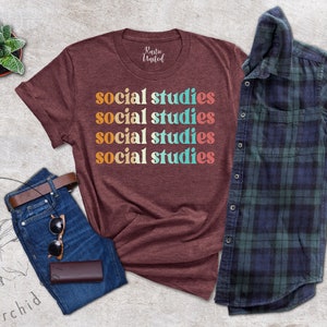 May include: A maroon t-shirt with the words "social studies" in a retro font. The shirt is paired with blue jeans, a brown belt, sunglasses, and a wallet. A green and brown plaid shirt is also included.