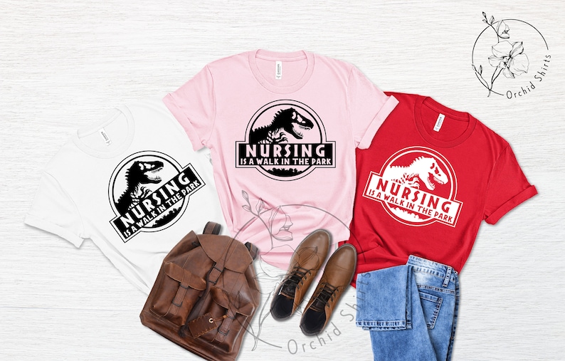 May include: Three t-shirts with a dinosaur graphic and the text "Nursing is a walk in the park". The shirts are white, pink, and red.
