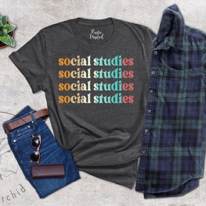 May include: Dark gray t-shirt with the words "social studies" in a retro font. The shirt is paired with blue jeans, a brown belt, sunglasses, and a wallet. A plaid shirt and a small potted plant are also in the image.